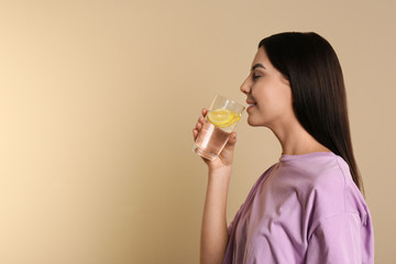 Sticker - Beautiful young woman drinking tasty lemon water on beige background. Space for text