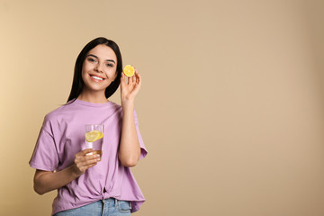 Sticker - Beautiful young woman with tasty lemon water and fresh fruit on beige background. Space for text