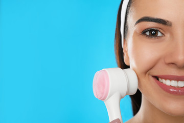 Canvas Print - Young woman using facial cleansing brush on light blue background, closeup with space for text. Washing accessory