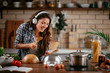 © JustLife - Young woman in kitchen. Beautiful woman singing and dancing while cooking. Woman listening music while cooking.