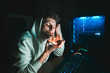 © bodnarphoto - Young gamer sits at home at the table at the computer and eats pizza. Young man eating pizza at break after computer game. Night gaming with fast food