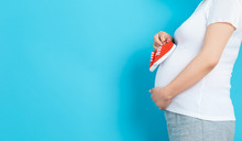 Pregnant Woman On A Solid Background Holding Baby Shoes