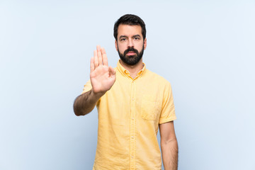 Young man with beard over isolated blue background making stop gesture