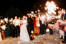 A Crowd Of Young Happy People With Sparklers In Their Hands During Celebration. Sparkler In Hands On A Wedding - Bride, Groom And Guests Holding Lights In Hand. Sparkling Lights Of Bengal Fires.