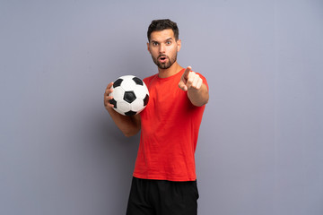 Handsome young football player man over isolated white wall surprised and pointing front