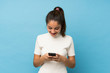 © luismolinero - Young brunette girl over isolated blue background sending a message or email with the mobile