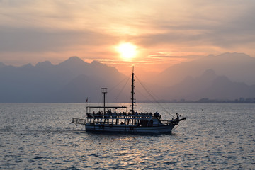 Wall Mural - Old ship in the sea at sunset. Mountains on the horizon.