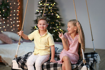 Boy and girl ride on a swing, communicate, laugh against the backdrop of New Year's decorations