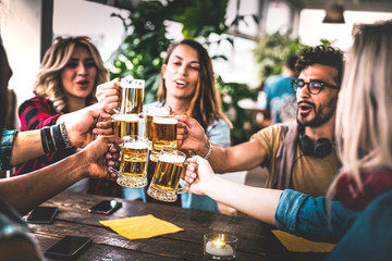 Friends toasting beer at brewery bar indoor at rooftop party - Friendship concept with young people having fun together drinking at happy hour promotion - Focus on glasses - Warm vignetting filter