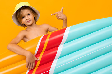 attractive European blond boy in a summer panama with an inflatable swimming mattress on a orange background