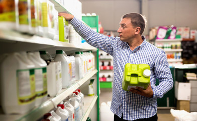 Man choosing liquid fertilizer in plastic bottle in hypermarket