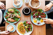 Different colorful meals for breakfast or lunch time on a plate with cutlery on woman's hands. Fried eggs, omelette, bruschetta and sausage on a wooden table in restaurant. Flat lay top view.