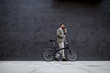 © Dusan Petkovic - Side view of handsome caucasian fashionable man in sweater pushing bike and talking on the phone while passing by gray wall.
