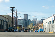 Homeless Tents On The Sidewalk Next To A Street And Portland Oregon City Skyline Seen In The Distance.