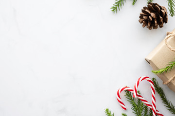 White marble table with Christmas decoration including giftbox, candy cane, pine branches and pine cones. Merry Christmas and happy new year concept. Top view with copy space, flat lay.