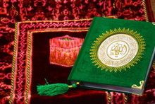 Green Al-Quran, Moslem Holy Book With Arabic Letters On A Red Praying Rug
