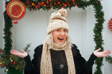 Funny winter portrait, beautiful young girl in knitted hat laughs on street on background of Christmas background. Happy New Year