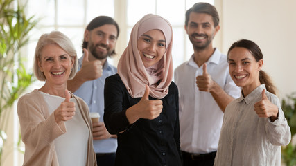 Head shot portrait of smiling multiracial group showing thumbs up.