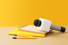 Microphone And Notebooks On Table Against Color Background