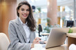 © ty - Portrait of a cheerful young businesswoman sitting at the table in office and looking at camera.