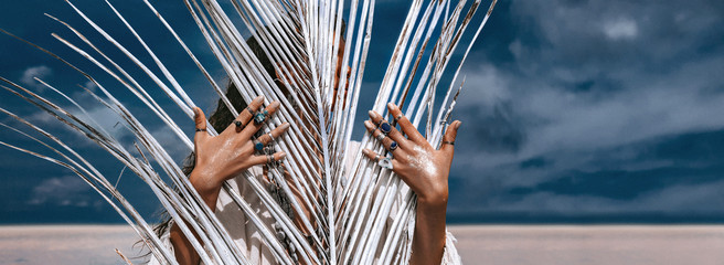 close up of beautiful young tribal style woman with lots of accessories behind painted white palm leaf