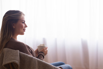 Wall Mural - Young peaceful girl enjoying cocoa near window at home