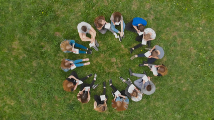 A group of students are sitting in a circle and books on the grass.