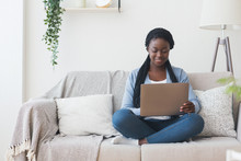 Black Millennial Woman Working With Laptop Computer On Sofa At Home