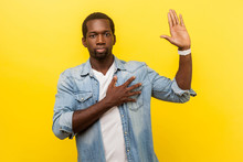 I Swear! Portrait Of Honest Serious Man In Denim Casual Shirt With Rolled Up Sleeves Keeping Hand On Chest And Raising Palm, Giving Promise, Pledge. Indoor Studio Shot Isolated On Yellow Background