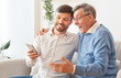 © Prostock-studio - Middle-Aged Son Showing Elderly Father How To Use Smartphone Indoor