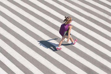 Schoolgirl crossing road on way to school. Zebra traffic walk way in the city. Concept pedestrians passing a crosswalk. Stylish young teen girl walking with backpack. Active child. Top view