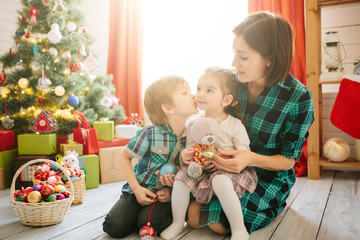 Wall Mural - Happy family mom, son and daughter on a Christmas winter sunny morning in a decorated Christmas celebration room with a Xmas tree and gifts.