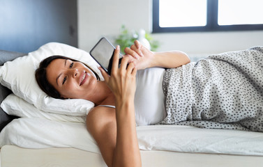 Wall Mural - Woman is using her smartphone while smiles lying on her bed.