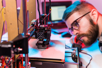 young male designer engineer using a 3d printer in the laboratory and studying a product prototype, 