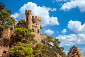 Wall Mural - Stone castle against blue sky with white clouds. Beautiful summertime travel destination on Balearic coast of Spain, the town of Lloret de Mar