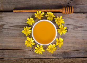 Wall Mural - honey in the glass bowl, dipper and yellow flowers around it on wooden background