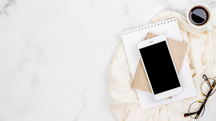 Wall Mural - Feminine home office desk concept. White marble background with smartphone, paper notepad, glasses, cup of coffee. Top view, flat lay, copy space.