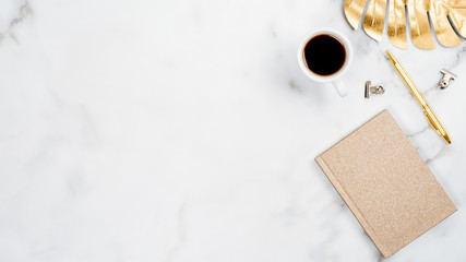 Wall Mural - White marble desktop with golden office accessories and stationery. Home office desk table with gold tropical monstera leaf, cup of coffee, paper notebook, pen. Flat lay style minimal layout. Top view
