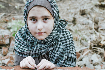 a refugee child in the war, a Muslim girl with a dirty face on the ruins, the concept of peace and war, the child is crying and waiting for help.