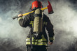 © alfa27 - rear view on fire fighter stand holding hammer isolated over smoky background, wearing red helmet
