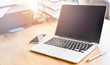 © Milan - Modern laptop with blank screen on table, Computer notebook workplace with cellphone and pen at wooden board.