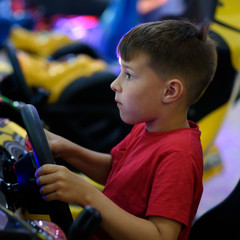 Wall Mural - Cute European boy in red t-shirt playing car racing on slot-machine. He enjoying his spare time