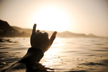 Silhouette Man Raises His Hand Out Of The Water Holding Up Two Fingers Up In The Sunset Time