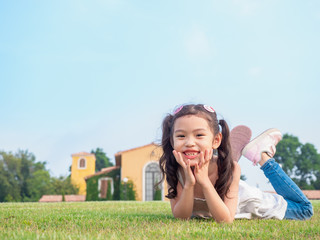 Little Asian cute girl 6 years old lying on the grass and smile at the lawn front of yard.