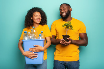Wall Mural - Happy couple hold a plastic container with bottles and a small tree over a light blue color. Concept of ecology, conservation, recycling and sustainability