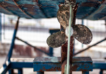 Rusty Propeller On A Blue Fishing Boat On A Harbour Dock. Boats Being Serviced In Dry Dock, Cleaned From Mossy Grass And Painted