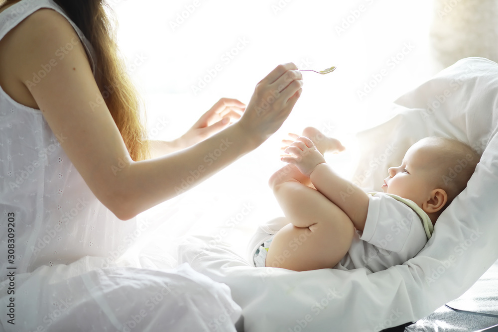 Maternity concept. A young mother feeds her little baby. First lure and breastfeeding. Family in white clothes. - obrazy, fototapety, plakaty 