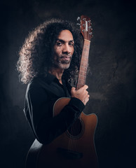 Portrait of attractive curly man with guitar at dark photo studio.