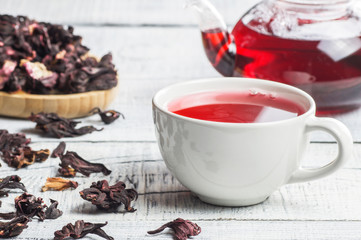 Wall Mural - White cup of healthy hibiscus tea with dried hibiscus flowers on white wooden background, winter hot drink concept for cold and flu 