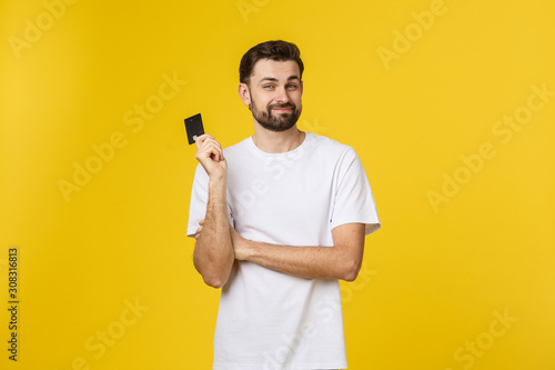 Fotomural Happy smiling young man showing credit card isolated on yellow background